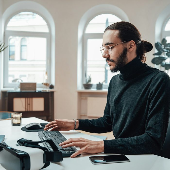 Bearded office worker with long hairs types on keyboard in office